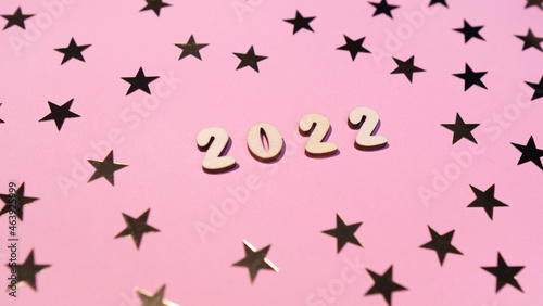 Cheerful wooden lettering happy new year 2022 on a soft gently pink background with gold stars. Sparkle confetti holiday concept  © Adelina