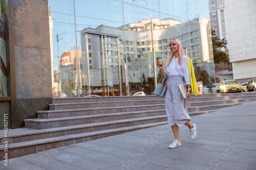 Cheerful woman with laptop walking on the street