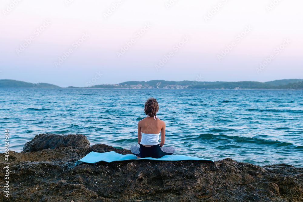 Girl sitting on a stone and looking at the sea at sunset