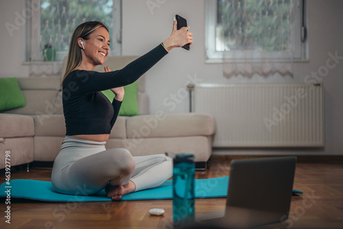 Young beautiful woman taking selfie with her smartphone while training at home
