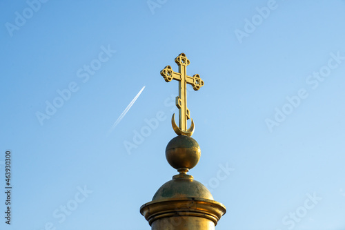 A golden Orthodox cross on a dome with a moon, an airplane flies across the blue sky. A sign. Orthodox church, temple .