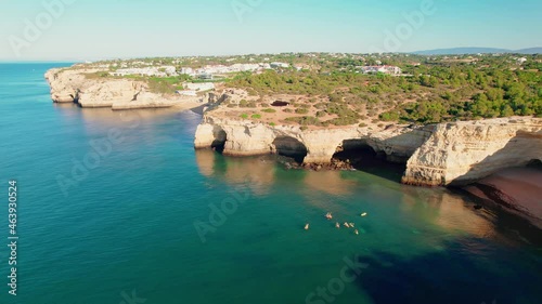Aerial view of Benagil Caves with kayaks swimming in blue oceanic waters in 4K. Algar de Benagil, coastal view from above on a beautiful sunny day with people relaxing on holiday in a residential area