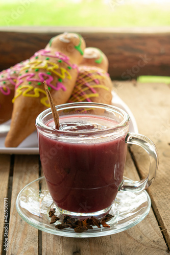 Traditional ecuadorian Colada morada and guaguas de pan on a rustic and warm set up. Purple juice and doll shaped bread. Ecuador's gastronomic culture. Day of the dead typical food and drinks concept.