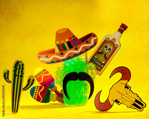 abstract background with mexican elements of sombrero, tequila, maracas, cactus and a glass mug in the form of a cactus on a yellow background, selective focus