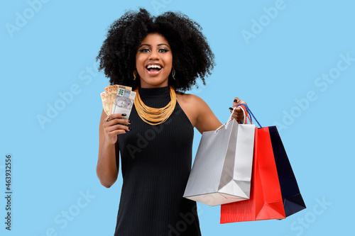 woman holding shopping bags holding Brazilian money, isolated cyan background