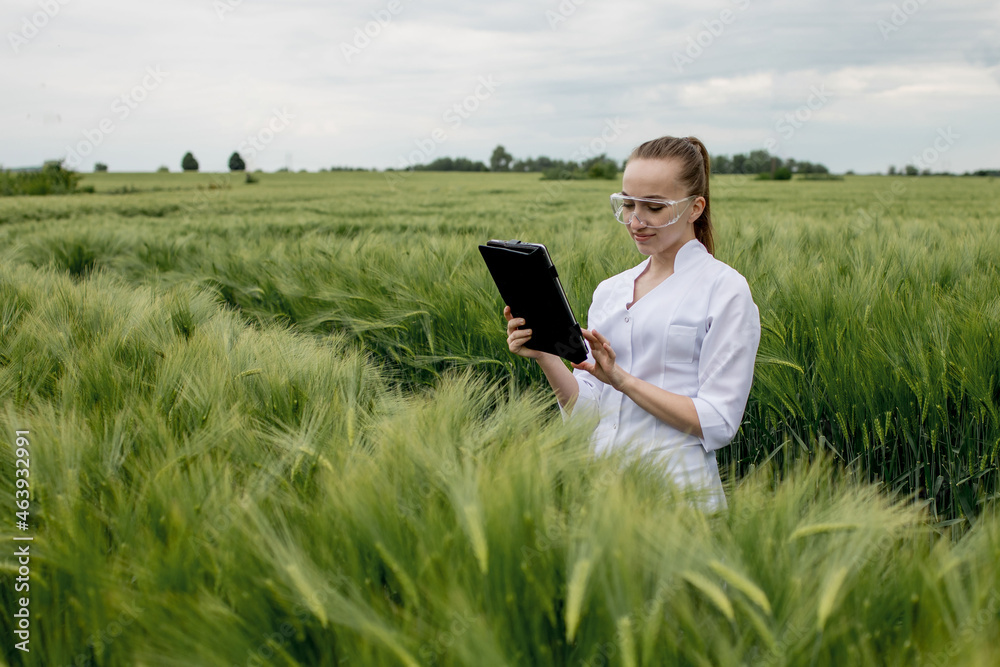 Young female ecologist scientist in goggles standing in green field and working on glass transparent screen Young female ecologist scientist in goggles standing in green field and working on glass transparent screen