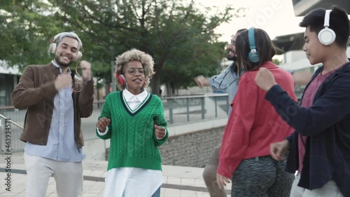 Multiracial group of funny friends dancing together while listening music with wireless headphones in city street - Silent disco headphones concept photo