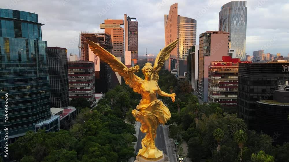 Toma aérea del monumento a la glorieta del ángel al amanecer con los rascacielos de la ciudad de México de fondo haciendo un paneo hacia abajo para revelar la base adornada de flor de cempasúchil 