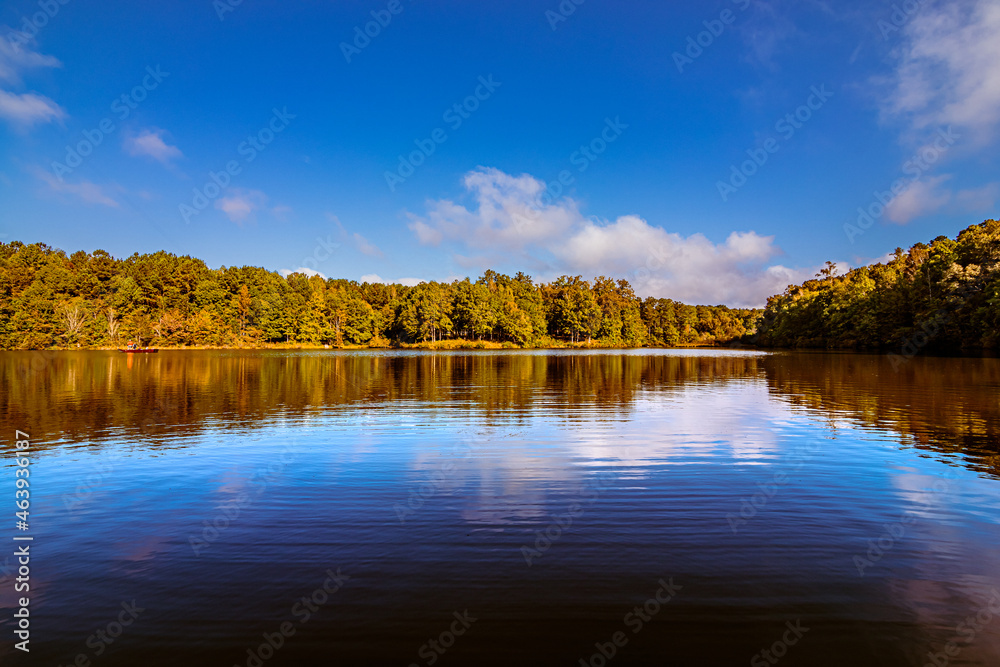 multi-colored autumn trees and leaves reflecting on lake with sky and cloud reflections in blue during fall season