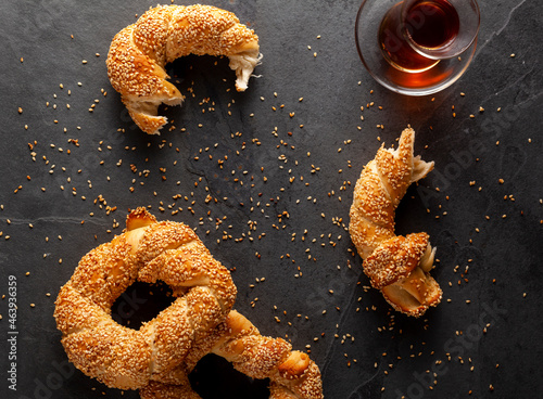 delicious Turkish bagel with sesame seeds known as susamli simit. Flat lay image shows whole and pieces of the bagels with sesame seeds and crumbles as well as a glass Turkish tea cup photo