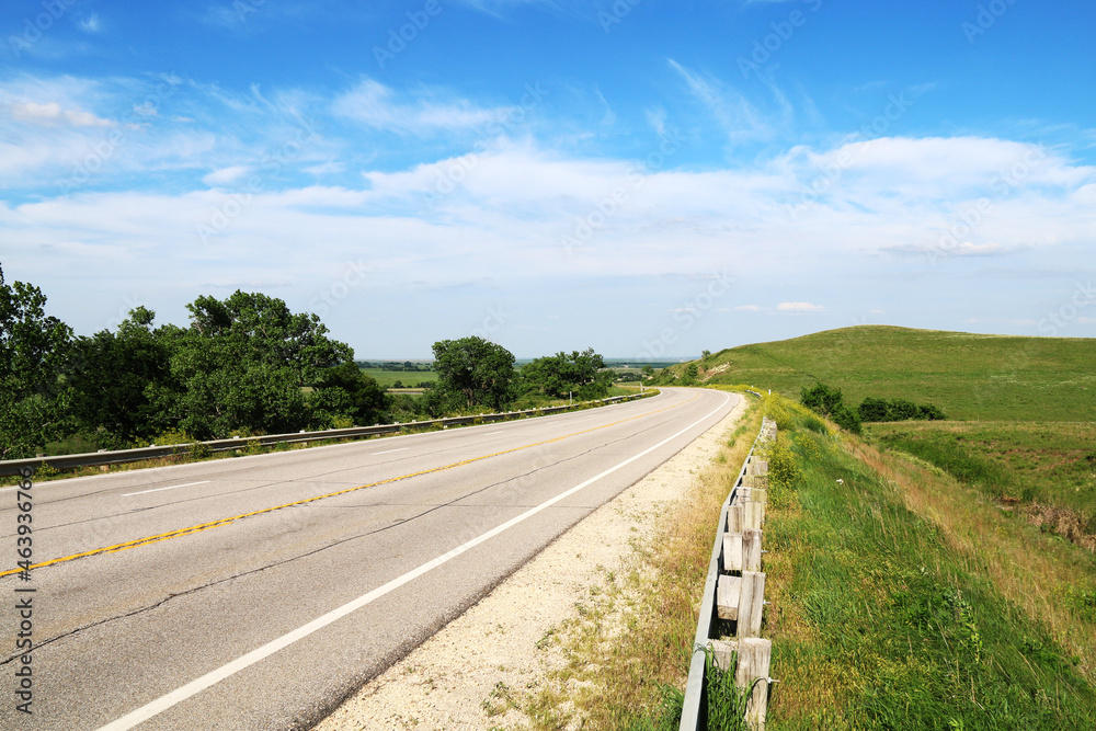 lonely road heading to distance with tree lined edge and green hills under a cloudy blue sky lonely road heading to distance with tree lined edge and green hills under a cloudy blue sky