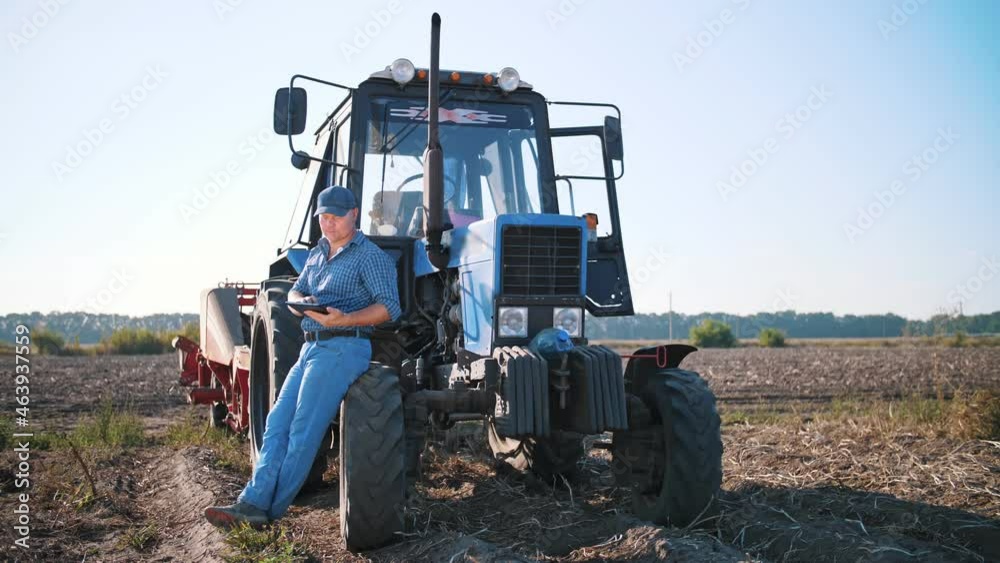 potato harvesting. farmer using digital tablet. on farm field, on farm machinery backdrop. tractor with potato harvester. smart farming. farming technologies potato harvesting. farmer using digital tablet. on farm field, on farm machinery backdrop. tractor with potato harvester. smart farming. farming technologies