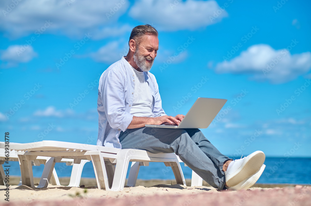 Man with laptop sitting on beach lounger