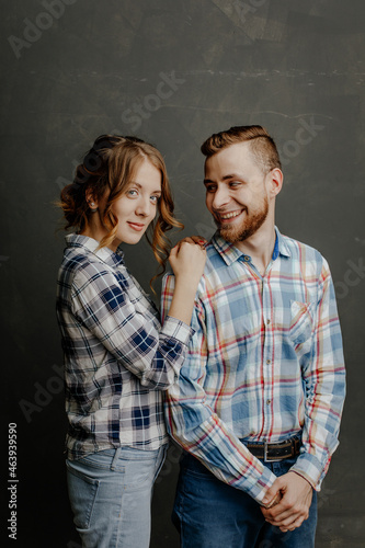 young couple in plaid shirts hugs on gray background