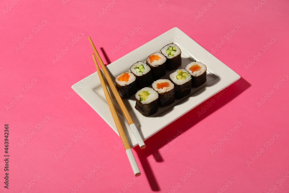 Plate with different maki rolls and wooden chopsticks on color background Plate with different maki rolls and wooden chopsticks on color background