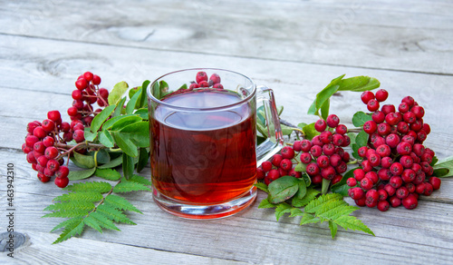 Still life with a glass of tea and rowan berries on a wooden background.