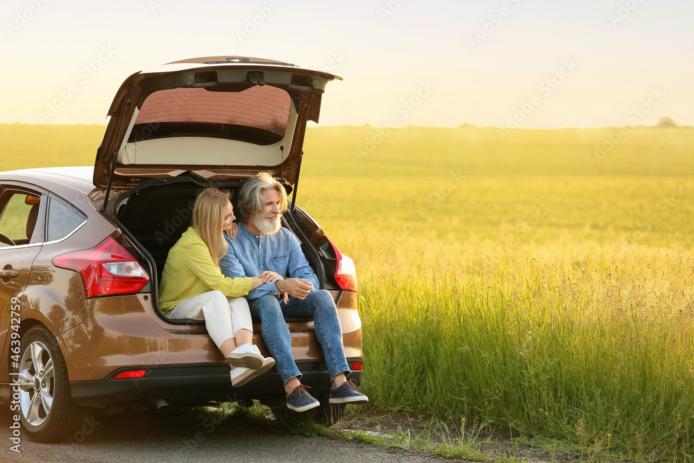 Happy mature couple sitting in car's trunk outdoors Happy mature couple sitting in car's trunk outdoors