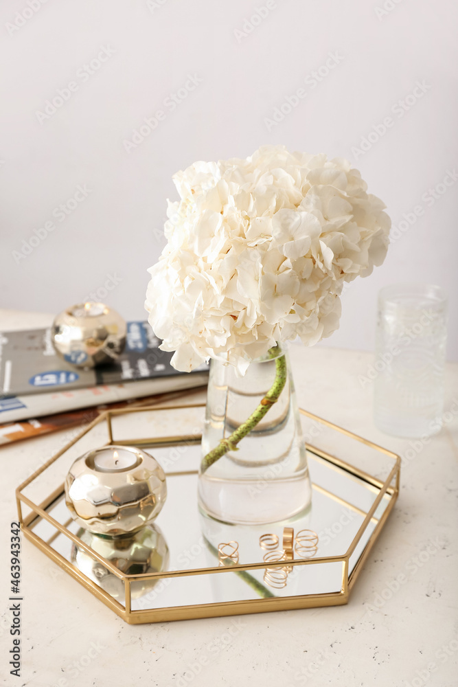 Beautiful hydrangea in glass vase and stylish decor on table in interior of light room - obrazy, fototapety, plakaty 