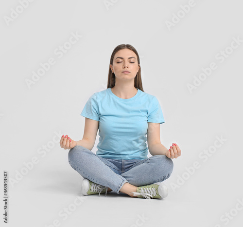 Young woman meditating on light background