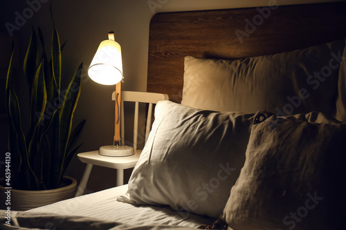 Fotografie Glowing lamp on bedside chair in dark room