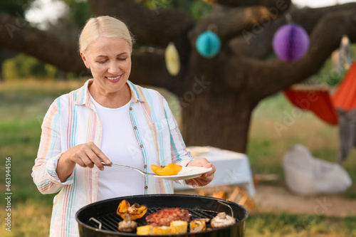 Mature woman cooking food on barbecue grill outdoors