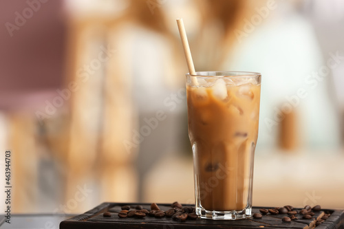 Glass of ice coffee with milk, straw and beans on table in room