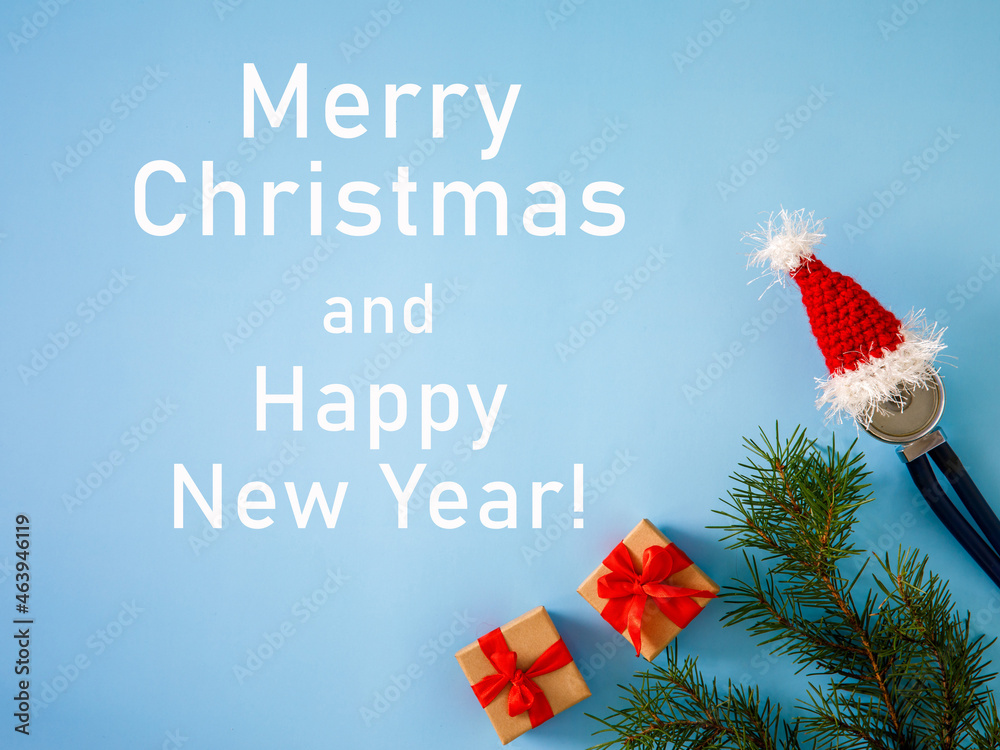 inscription Merry Christmas and Happy New Year medical banner, gift boxes, stethoscope in Santa hat and Christmas tree on blue background. Close-up. Top view, flatlay, greeting card