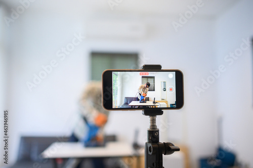 A young Asian man uses a metal cutter and records video via smartphone. Young man broadcasting via smartphone. Focus with smartphone.
