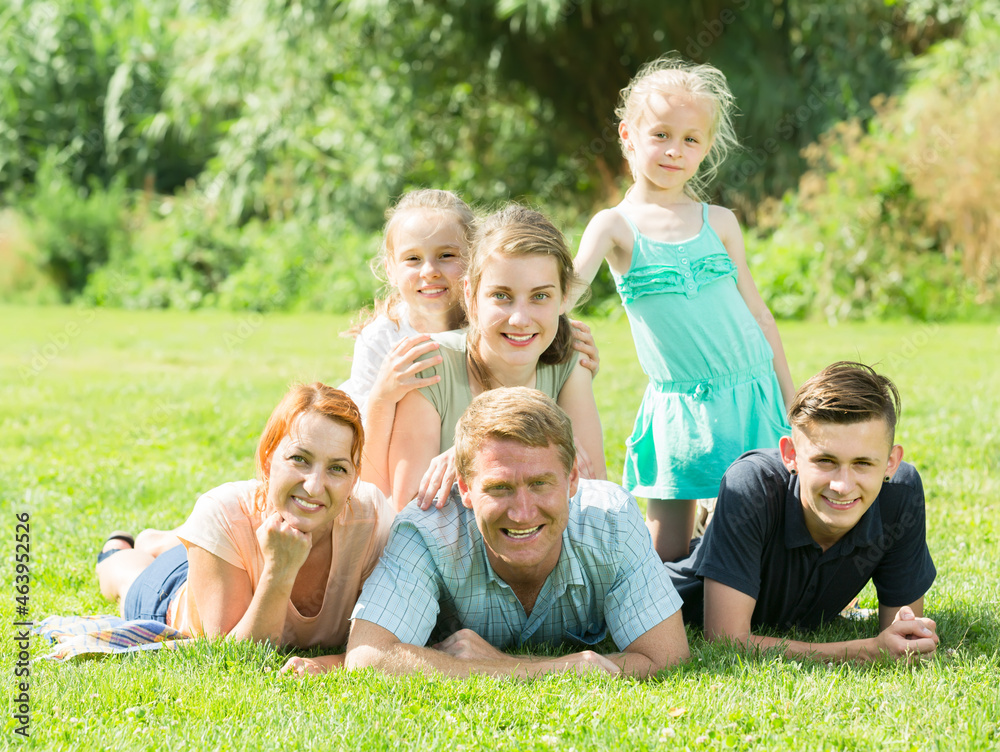 Fototapeta premium Portrait of big family with parents and four children lying together on green lawn outdoors