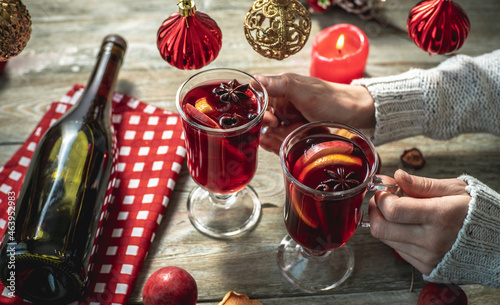Woman in a sweater is holding couple glasses with fragrant hot mulled wine decorated with fruits and spices. Concept of a cozy holiday atmosphere, New Year and Christmas mood