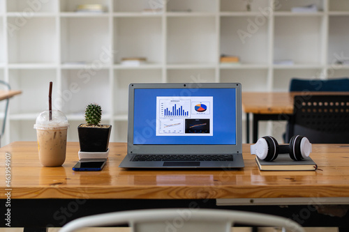 Laptop notebook with graphs on wooden table with notebook, smartphone, and music headphones or podcast background with coffee in the modern workplace.
