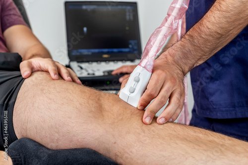 Close-up of a physiotherapist performing an ultrasound of the knee on a patient lying on the stretcher