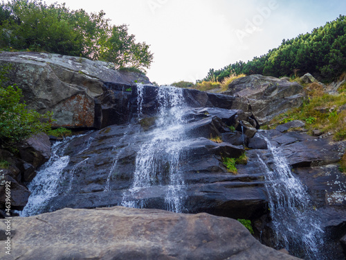 Summer landscape in the mountains. Waterfall under the peak of Hoverla  stormy clean water feeds the river Prut on the background of wild mountain slopes of the Carpathian Mountains. 