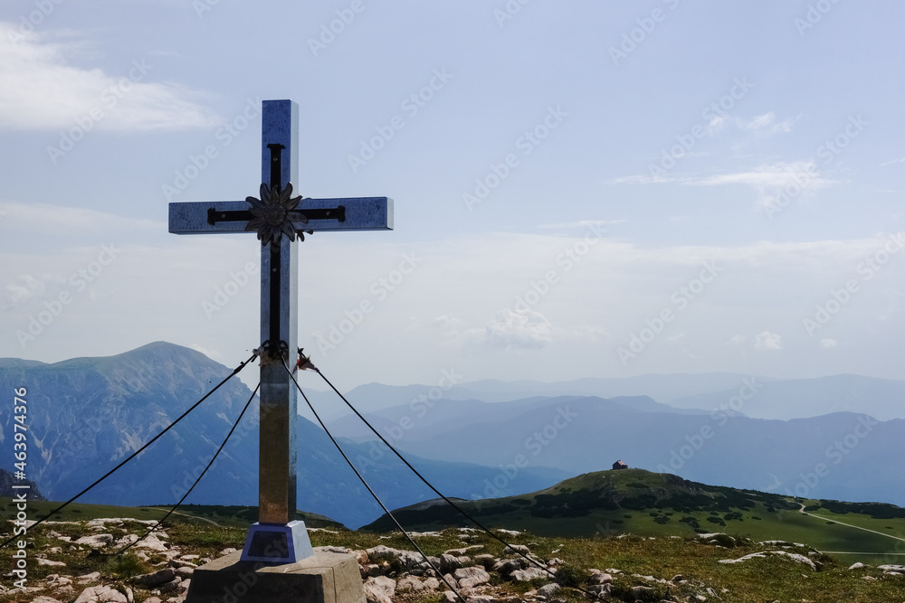 summit cross and a alpine hut on the top from a green hill with blue sky