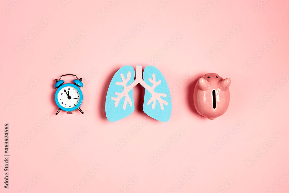 Lungs symbol with alarm clock and piggy bank on pink background. Save money for treatment and lung care.