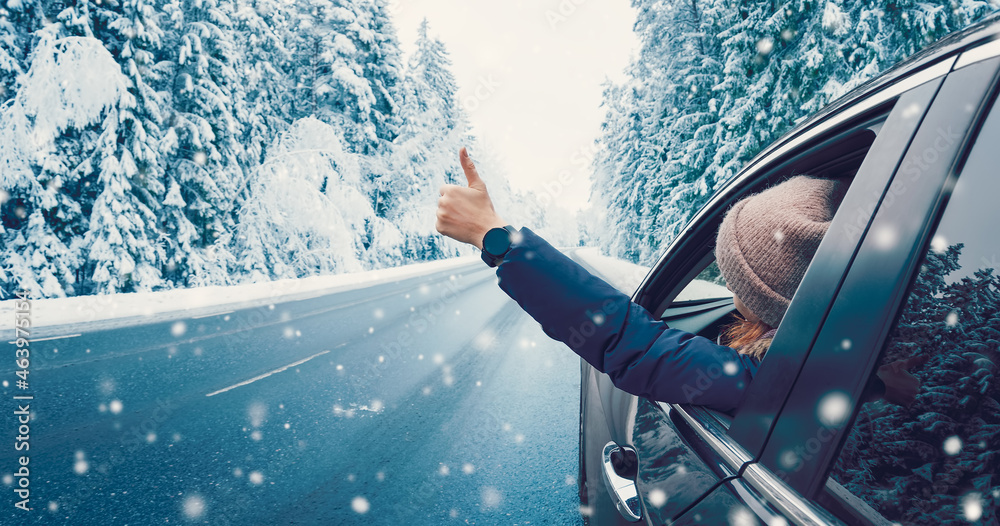 Happy woman in the car gesture finger up on the snowy background. - obrazy, fototapety, plakaty 