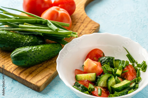 cucumber and tomato salad in a white bowl next to a cutting board with vegetables