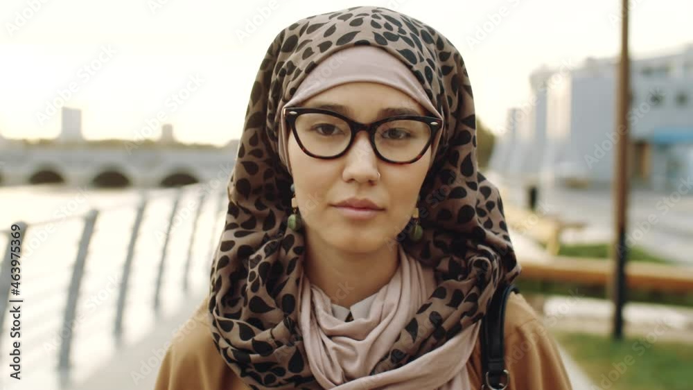 Shoulder-up POV of young Middle Eastern Muslim woman wearing hijab, looking on camera, standing outdoors at daytime Shoulder-up POV of young Middle Eastern Muslim woman wearing hijab, looking on camera, standing outdoors at daytime