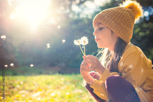Valokuvatapetti Little beautiful girl blowing dandelion on the meadow at sunset