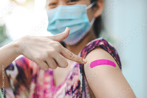 A healthy tourist woman pointing to her pink Plaster Bandage after getting the corona vaccine vaccinated immunity is wearing a protective face mask. Vaccination inoculation concept. Selective focus