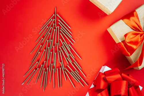 Long golden self-tapping screws, laid out in shape of Christmas tree, and gift boxes on red background