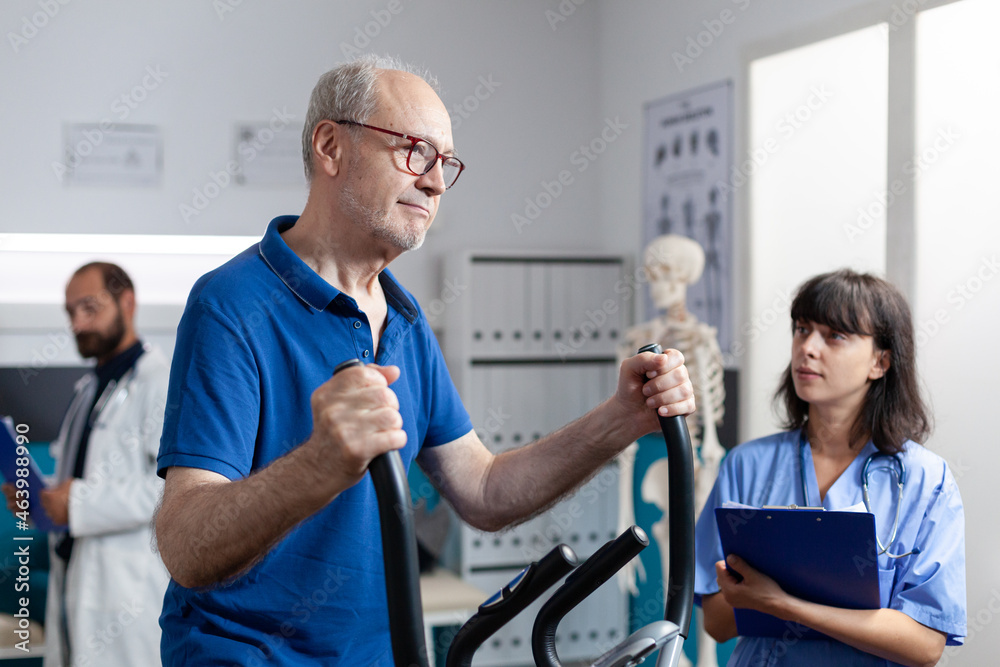 Obraz premium Senior man doing physical exercise for orthopedic recovery, receiving medical assistance from nurse at clinic. Old patient with leg injury training and doing gymnastics to recover.