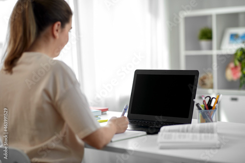 education, online school and distant learning concept - female student woman with laptop computer, notebook and book at home