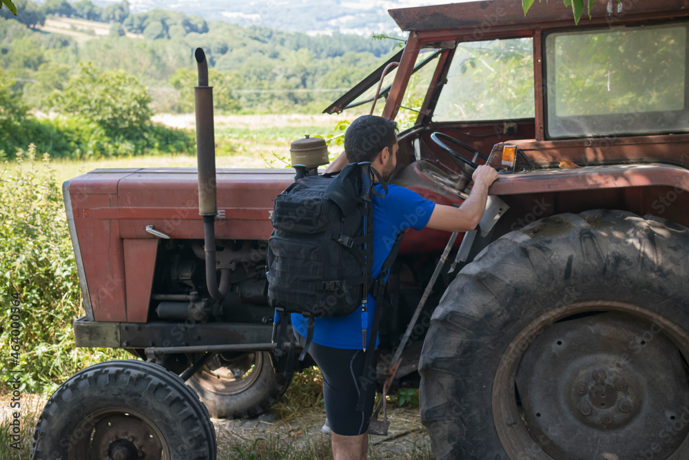 Hombre joven peregrino realizando el camino de Santiago montado en un tractor viejo y rojo Hombre joven peregrino realizando el camino de Santiago montado en un tractor viejo y rojo