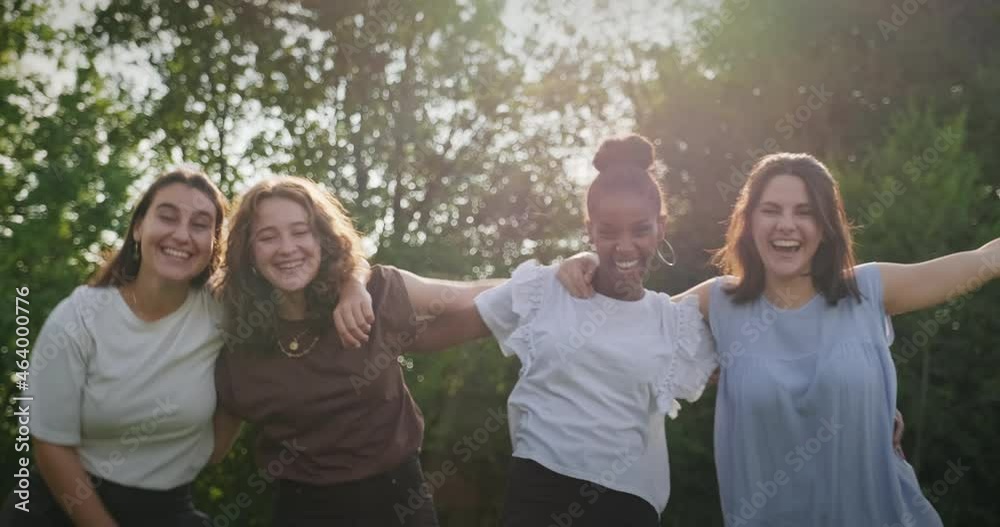 Youth culture with happy young people, group of female friends in park. Multiethnic teens outdoors, women smiling and laughing. Portrait of teenagers together, girls looking at camera. Slow motion