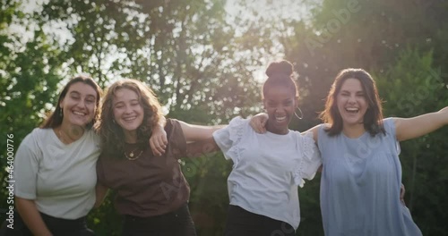 Youth culture with happy young people, group of female friends in park. Multiethnic teens outdoors, women smiling and laughing. Portrait of teenagers together, girls looking at camera. Slow motion photo