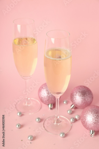 Glasses of champagne and baubles on pink background