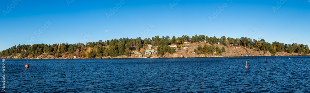 Swedish coast in autumn. Beautiful colorful panoramic view of the rocky shores of the Baltic sea bay with golden leaves trees and evergreens pines. Wooden traditional houses villas on the shore.