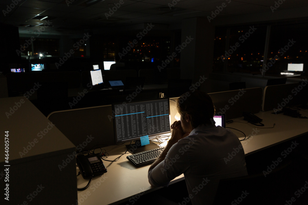 Caucasian male programmer sitting at desk, using computer with coding on screen Caucasian male programmer sitting at desk, using computer with coding on screen