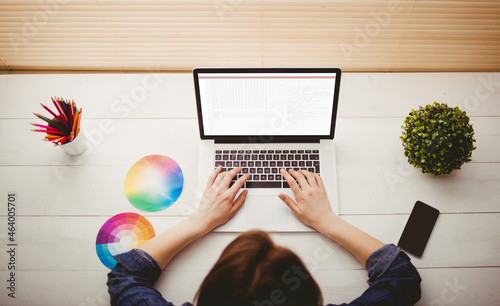 Hands of caucasian female programmer with colour charts using laptop with coding on screen